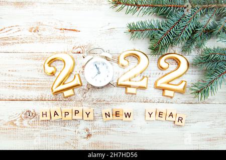 Candele sotto forma di numeri 2022, sveglia che mostra la mezzanotte, albero di Natale rami su uno sfondo di legno. Iscrizione con lettere in legno Foto Stock