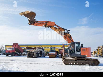 Nel cantiere è presente una grande macchina da lavoro, un escavatore cingolato. Un potente escavatore arancione con benna sollevata sullo sfondo Foto Stock