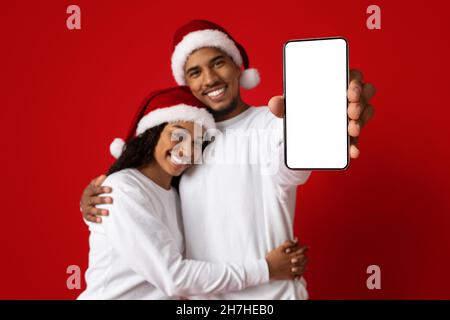 Amorevole coppia nera in Babbo Natale cappelli mostrare cellulare, mockup Foto Stock