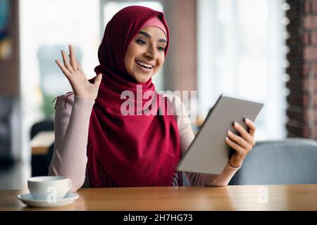Ragazza musulmana allegra in hijab che ha una chat video, usando un tablet Foto Stock