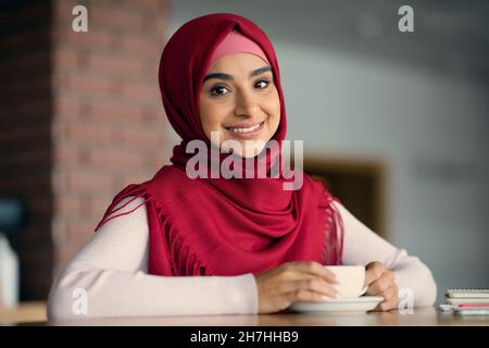 Attraente donna musulmana in hijab in posa al bar Foto Stock