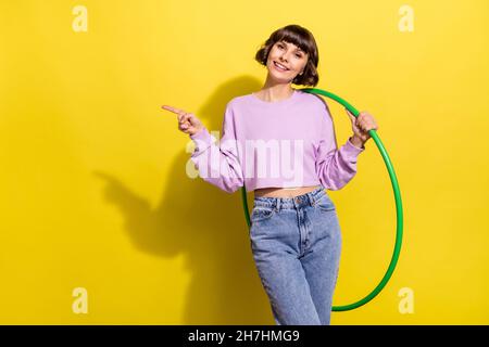 Ritratto di attraente ragazza allegra trendy che tiene hula hoop mostrando spazio copia isolato su sfondo giallo brillante Foto Stock