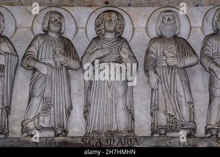 Santa Maria, fiancheggiata dagli Apostoli, scolpita dal maestro scultore lombardo del XIII secolo Guido Bigarelli o Guido da Como sull'architrave del portale centrale romanico sotto l'imponente portico sul fronte inferiore occidentale, in Piazza San Martino, della Cattedrale o del Duomo di San Martino in Lucca, Toscana, Italia. Foto Stock