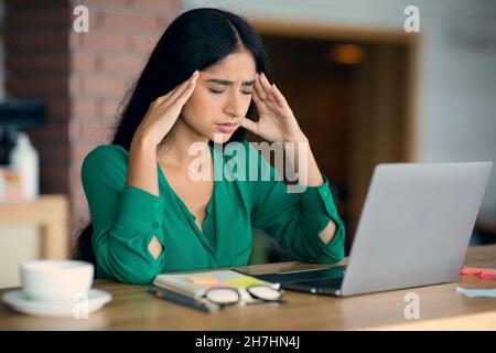 Stressata giovane donna arabica usando il laptop al caffè Foto Stock