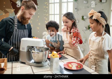 Uomo che mescola la farina in mescolatore e bambini che guardano per il processo di cottura in cucina Foto Stock