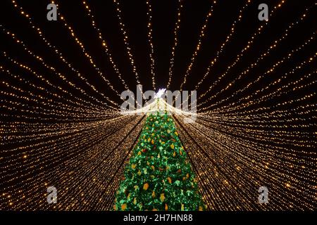 Bellissimo albero di Natale circondato da molte ghirlande e decorato con diversi baubles colorati e giocattoli. Foto di Capodanno con sfondo nero. Foto Stock