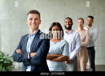 Uomo d'affari e donna d'affari di successo diversi che posano insieme sopra il muro grigio in ufficio Foto Stock