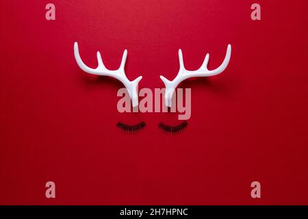 Faccia di renna di Natale fatta di ciglia e corna bianche su sfondo rosso. Minimo Natale o Capodanno concetto. Foto Stock