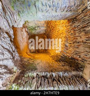 Piccolo corridoio o tunnel tra pareti, pavimento e soffitto di pietre deteriorate, muschio e illuminato con luce gialla, parete sullo sfondo, cast Foto Stock