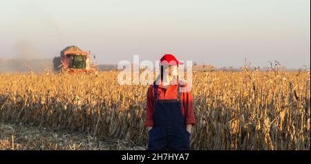 Giovane contadina nel campo del mais. Macchine agricole in background Foto Stock