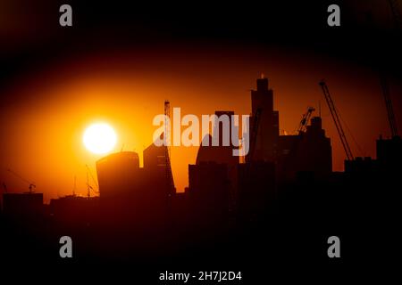 Il sole tramonta dietro le gru di costruzione e lo skyline del quartiere finanziario di Londra. Data foto: Martedì 23 novembre 2021. Foto Stock