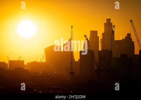 Il sole tramonta dietro le gru di costruzione e lo skyline del quartiere finanziario di Londra. Data foto: Martedì 23 novembre 2021. Foto Stock