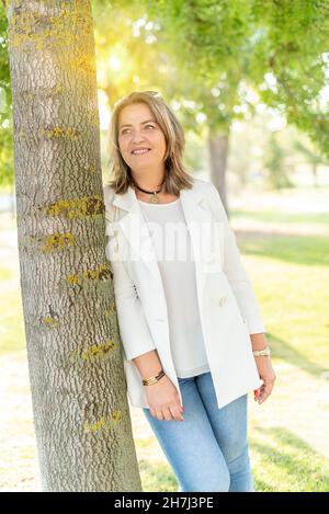 Ritratto di una donna caucasica di mezza età in abiti casual appoggiati ad un albero Foto Stock