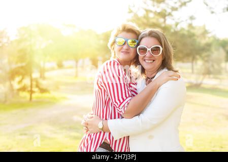 Ritratto di due donne caucasiche di mezza età che abbracciano e sorridono per celebrare la loro amicizia. Foto Stock