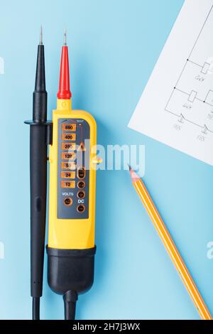 Indicatore di tensione giallo con uno schema elettrico su sfondo blu. Test e verifica delle reti elettriche Foto Stock