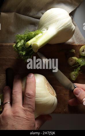 Primo piano di un finocchio per affettare un uomo su un tagliere di legno. Sfondo scuro. Direttamente sopra. Foto Stock