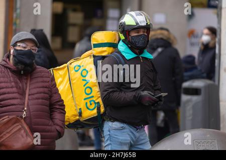 Madrid, Spagna - 27 dicembre 2020: Un addetto alla consegna di cibo, il pilota, della società Glovo, utilizza il suo cellulare per svolgere il suo lavoro Foto Stock