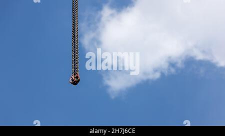 ganci appesi alle grandi catene della gru che discendono dall'alto, cielo blu nuvoloso sfondo Foto Stock