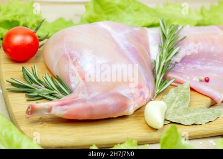 Carne cruda di coniglio rosa non cotta con rosmarino verde e verdure fresche su fondo di tagliere di legno chiaro. Foto Stock