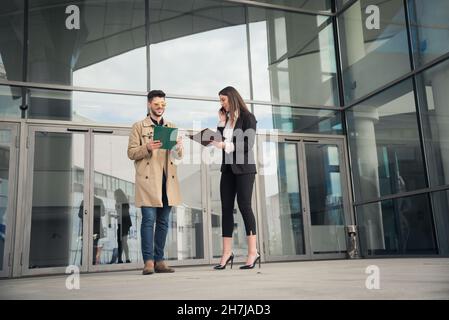 Il capo femmina e il suo assistente maschio stanno sorridendo insieme mentre sta parlando al telefono di fronte all'azienda Foto Stock