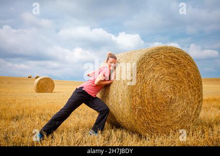 giovane donna che spinge in un campo di balle di paglia Foto Stock