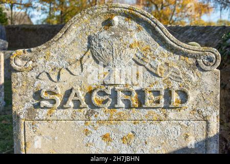 'Sacred' arruolato su un'antica pietra nel cimitero, la chiesa di San Pietro, Church Street, Yaxley, Cambridgeshire, Inghilterra, Regno Unito Foto Stock