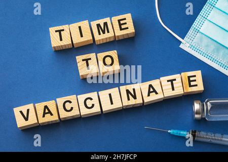 Cubi di legno con testo e forniture mediche su sfondo blu, tempo di vaccinare concetto Foto Stock