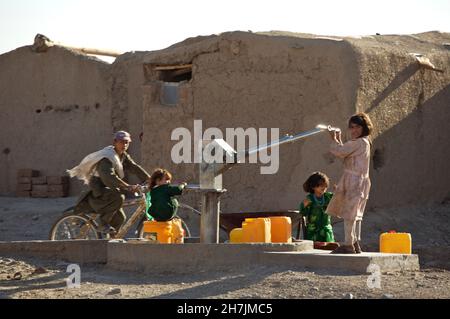 I bambini afghani raccolgono acqua potabile da una pompa a mano, nel campo di Maslakh per gli sfollati interni, alla periferia della città nord-occidentale o Foto Stock