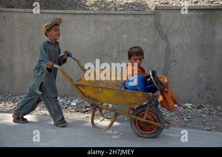 Un giovane ragazzo ruota il fratello più giovane con una bombola di gas GPL su un carrello. Lavora come giornalista a Torkham, una città vicino alla bord Pakistan-afghana Foto Stock