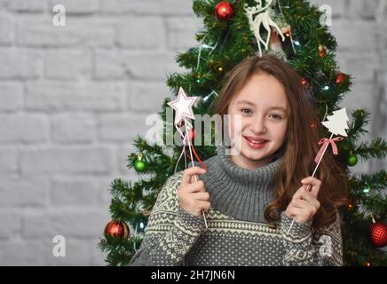 La ragazza ride e si rallegra sullo sfondo di un albero di Natale e di un muro di mattoni, contiene giocattoli di Natale Foto Stock