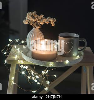 Un vaso con fiori bianchi secchi, una tazza di smalto grigio con un cuore disegnato con il tè, un candela che brucia su un vassoio per San Valentino. Spazio di copia. Luogo Foto Stock