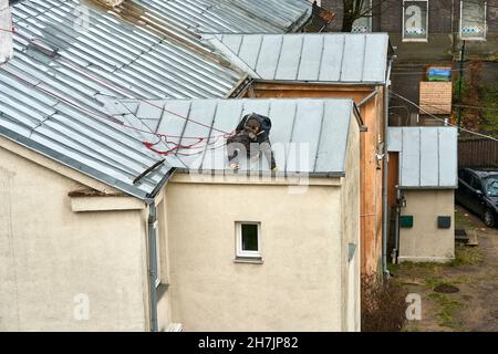 Un uomo legato con una corda rossa per la pulizia di sicurezza di un tubo di scarico sul tetto di una casa. Foto Stock