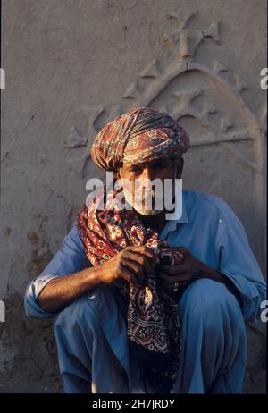 Un anziano Sindhi siede per un motivo sul muro della sua casa di fango, a Mithi, un villaggio nel deserto di Tharparkar della provincia di Sindh, in Pakistan. Luglio Foto Stock