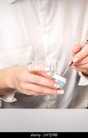 Smalto per unghie con glitter blu e spazzola per unghie nelle mani di un manicurista femminile Foto Stock