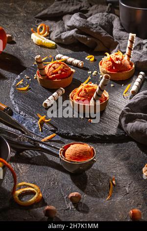 Gelato all'arancia fatto in casa su sfondo scuro con cucchiaio da gelato in acciaio inossidabile, fuoco selettivo Foto Stock