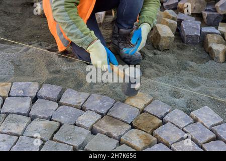 Primo piano del lavoratore di costruzione che installa pietre di pavimentazione posate sul marciapiede vicino alla strada Foto Stock