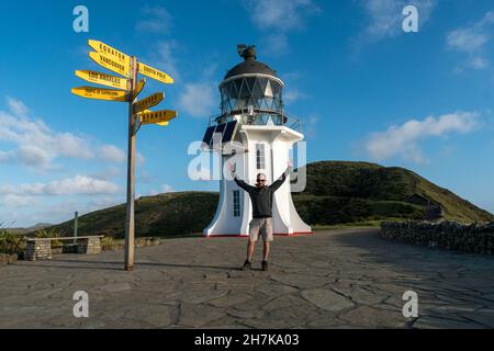 Uomo in piedi di fronte a un faro Capo Reinga sull'Isola del Nord della Nuova Zelanda al tramonto Foto Stock