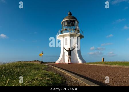 Uomo in piedi di fronte a un faro Capo Reinga sull'Isola del Nord della Nuova Zelanda al tramonto Foto Stock