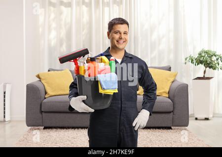 Pulitore maschio in un uniforme che tiene un secchio dei rifornimenti di pulizia in un soggiorno Foto Stock