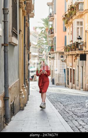 La donna alternativa con una parrucca verde guarda il suo telefono per strada Foto Stock