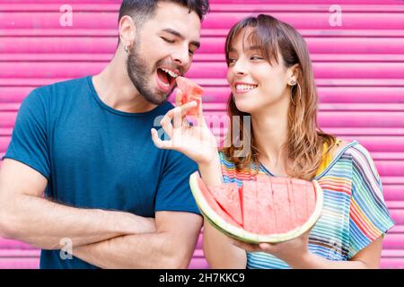 Uomo che mangia cocomero mentre la donna urla sullo sfondo Foto Stock