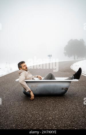 Uomo maturo che si rilassa in vasca da bagno su strada durante l'inverno Foto Stock