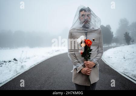 Uomo maturo avvolto in plastica che tiene mazzo di fiori su strada Foto Stock