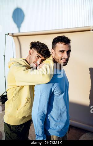 Sorridente giovane uomo che si appoggia su un amico maschio durante la giornata di sole Foto Stock