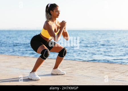 Giovane sportivo femminile che fa squat durante la giornata di sole Foto Stock