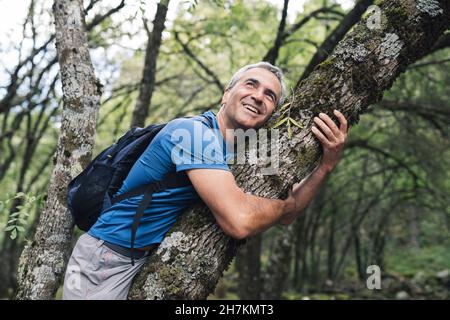 Uomo maturo che abbraccia albero in foresta Foto Stock