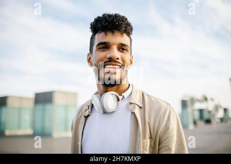 Giovane uomo sorridente con capelli ricci indossando cuffie wireless Foto Stock