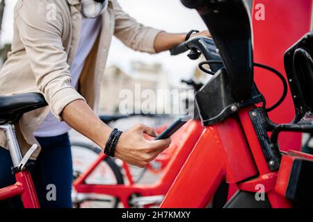 Uomo che sblocchi la bicicletta attraverso lo smartphone presso la stazione di parcheggio Foto Stock