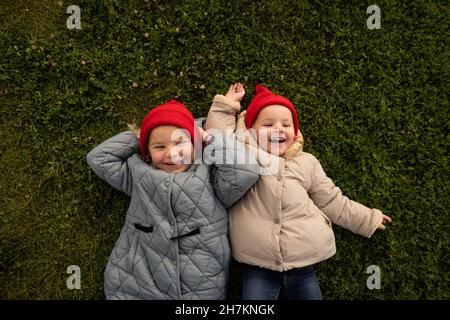 Sorelle giocose in abiti caldi giacenti sull'erba Foto Stock