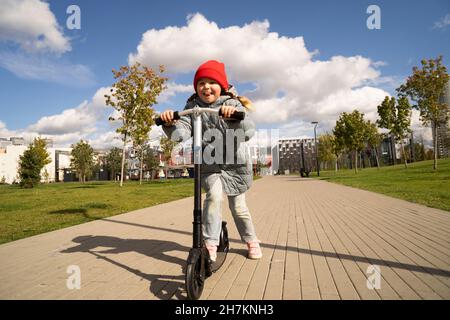 Ragazza che guida scooter giocattolo sul sentiero al parco durante la giornata di sole Foto Stock